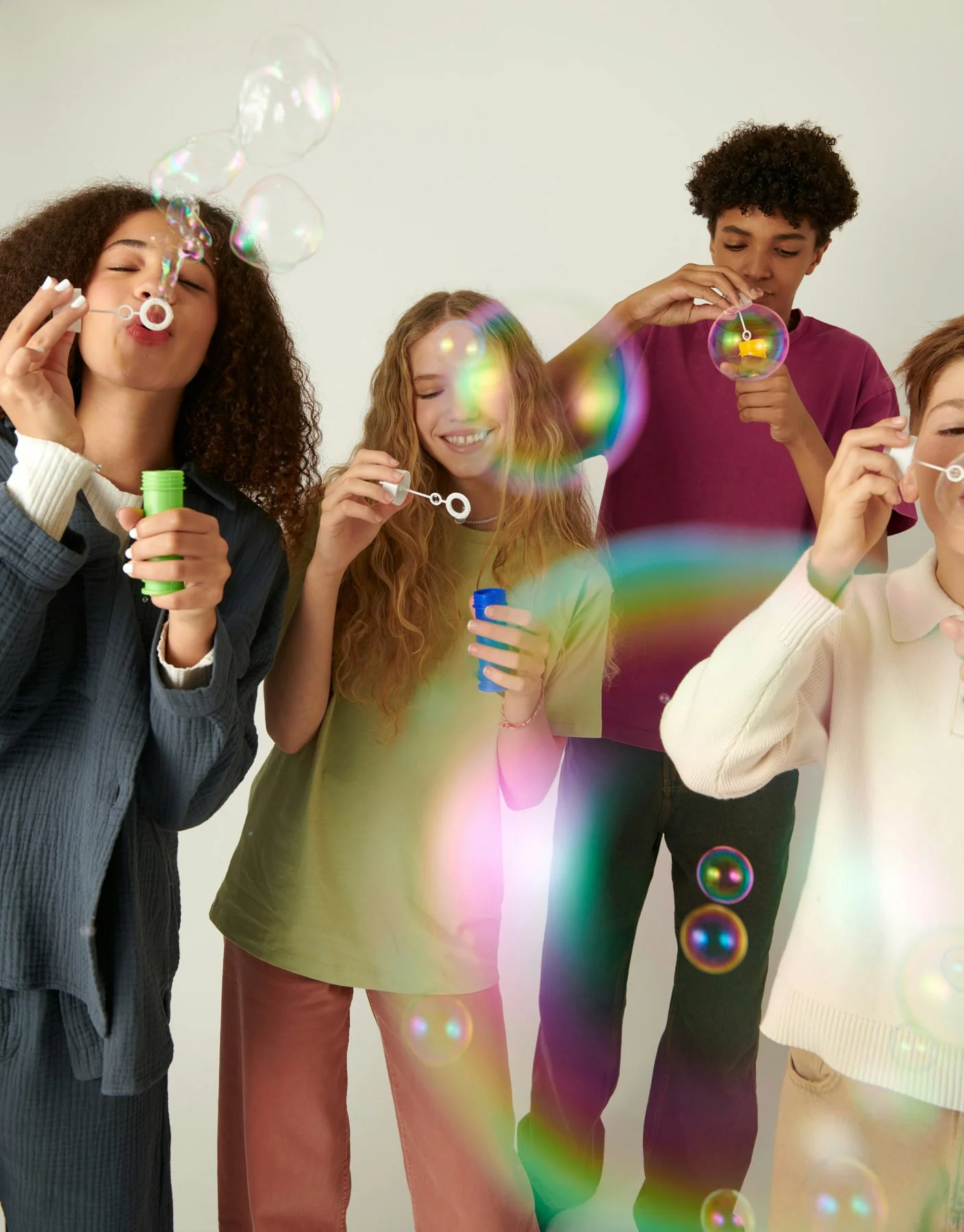Group of four friends blowing bubbles in a bright, plain room.