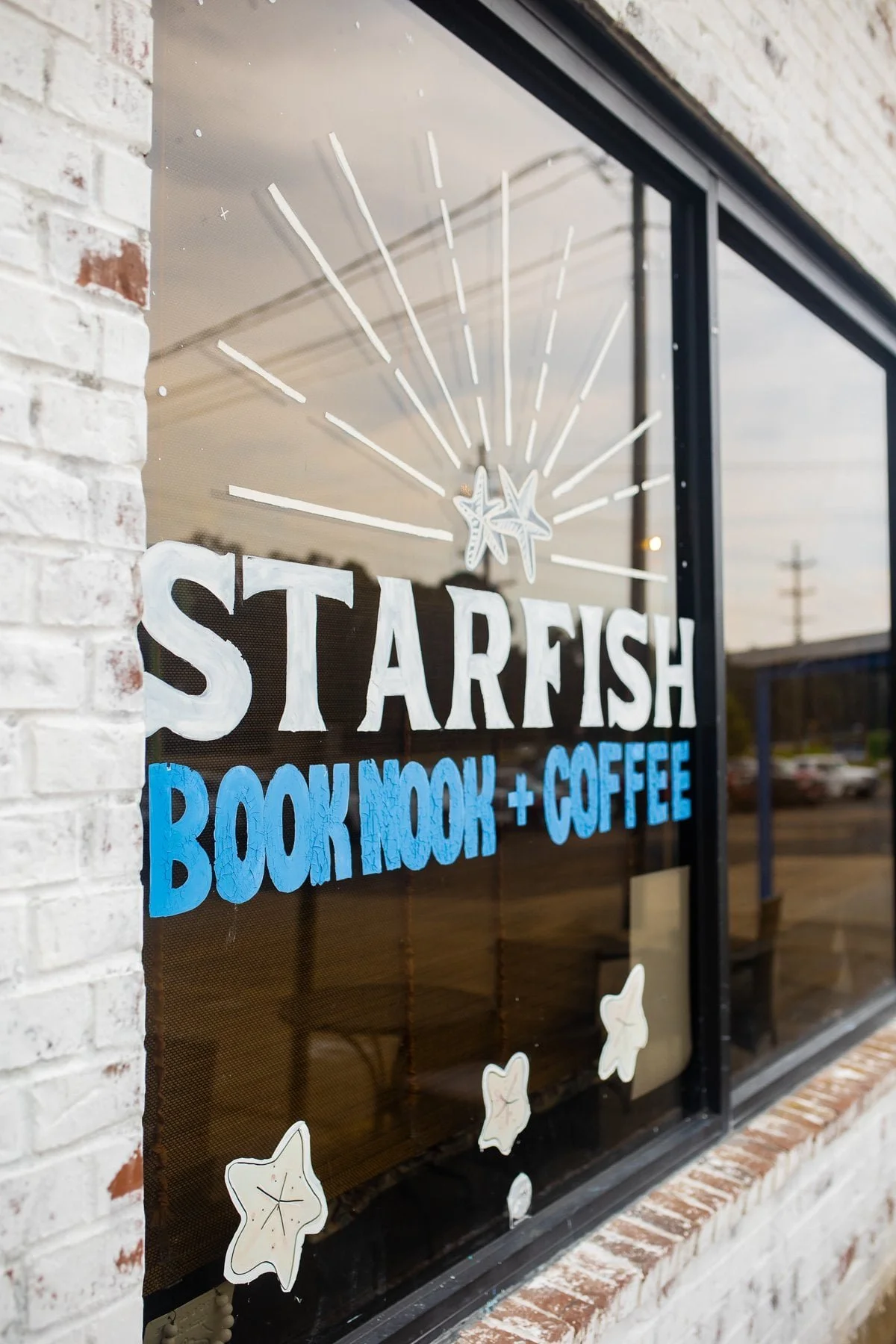 A storefront window with a sign that reads "Starfish Bookshop + Coffee" in white and blue letters. The window is decorated with starfish illustrations and is set in a brick wall.