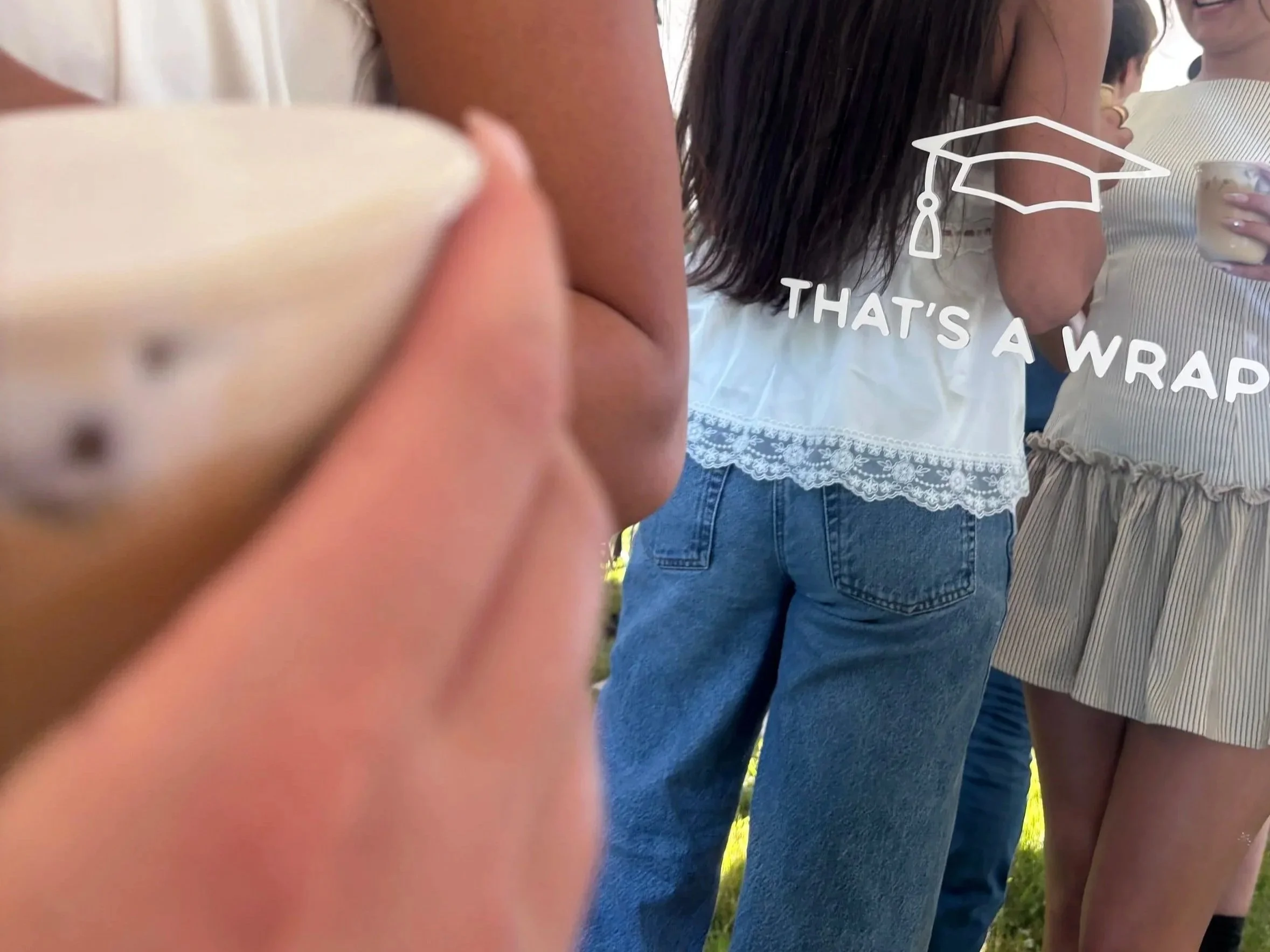 A group of people standing closely together outdoors, with some holding drinks, and a graphic of a graduation cap and the caption 'That's a wrap' overlaid.