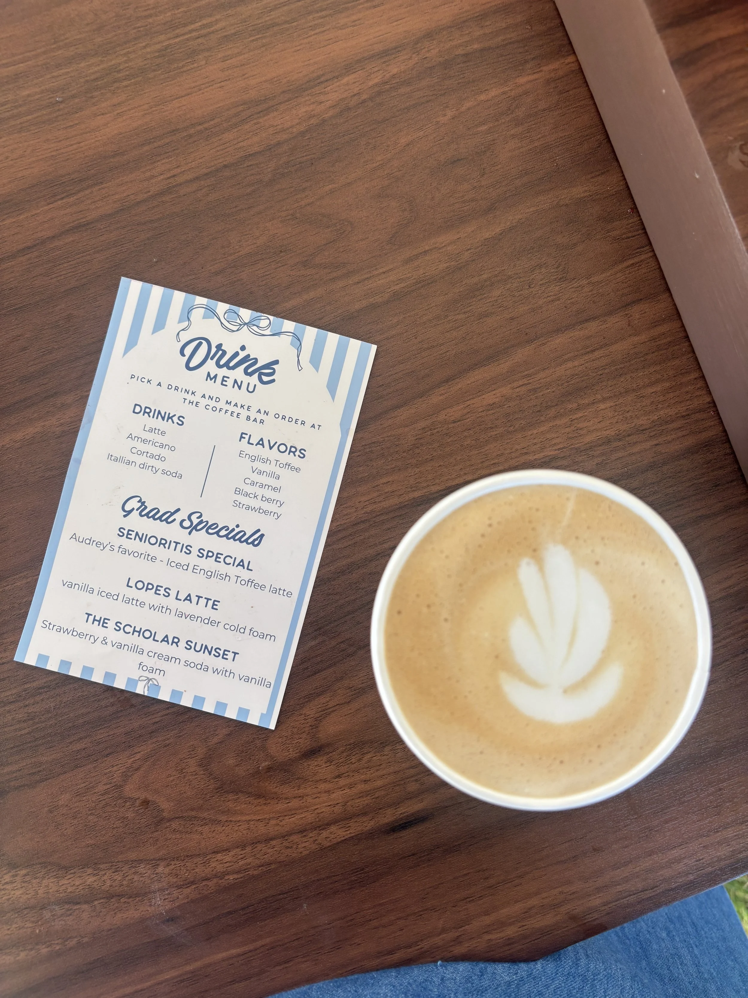 A coffee cup with latte art on a wooden table next to a drink menu with various beverage options.