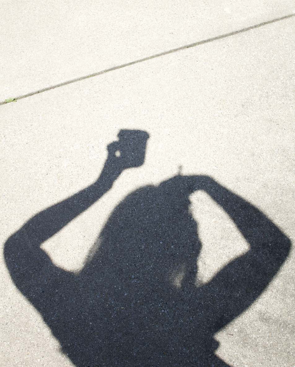 Shadow of a person taking a photo with a smartphone on concrete ground.