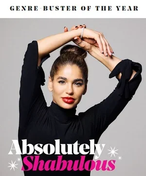 Close-up of a woman with dark hair in a bun, wearing a black top, with arms raised and hands clasped above her head. Text on the image reads 'GENRE-BUSTER OF THE YEAR' at the top and 'Absolutely Shabulous' at the bottom in white and pink letters.