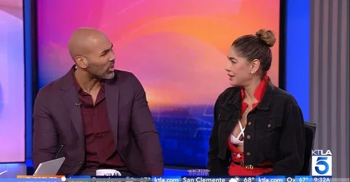 A man and woman are sitting and talking on a television set with a colorful background.