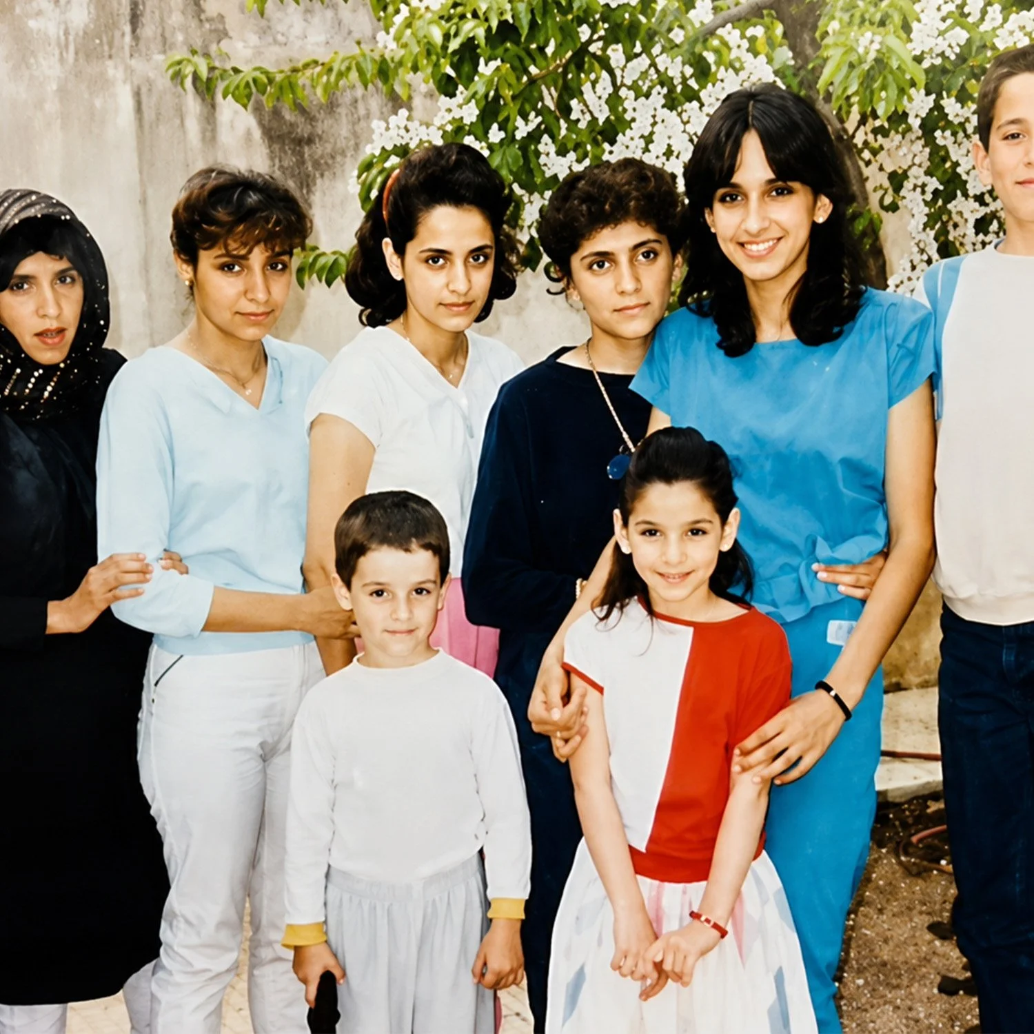 Group of people, including children and women, standing outdoors in front of a tree with white flowers, smiling for the photo.
