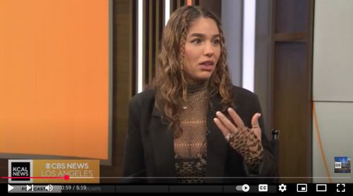 A woman with wavy brown hair and a leopard print glove speaking during a televised interview.