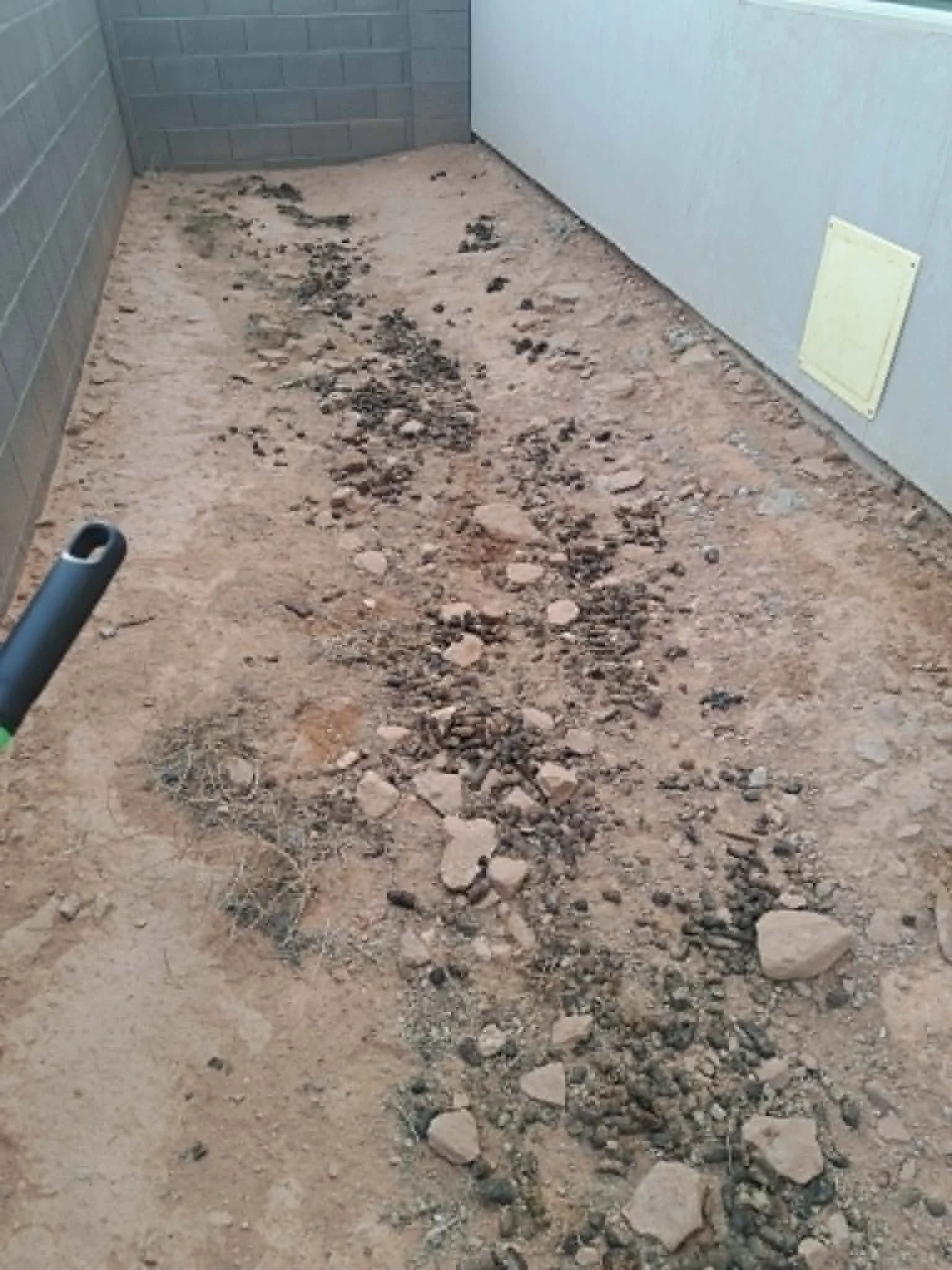 A floor with dirt, rocks, and debris in a corridor with a gray cinder block wall and a white door.