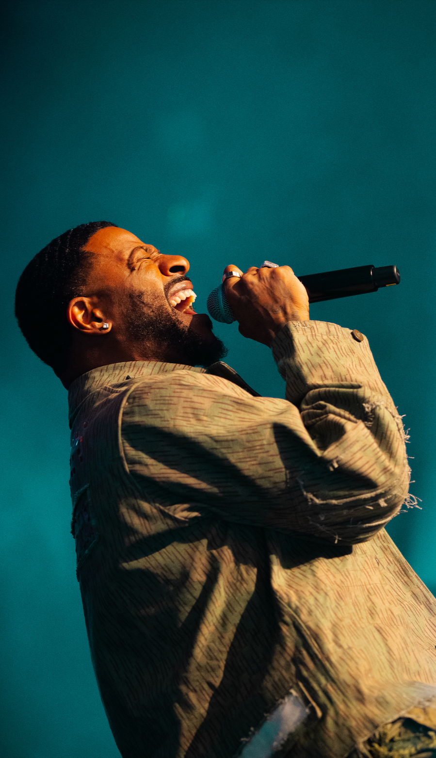 A male singer passionately performing with a microphone against a teal background.