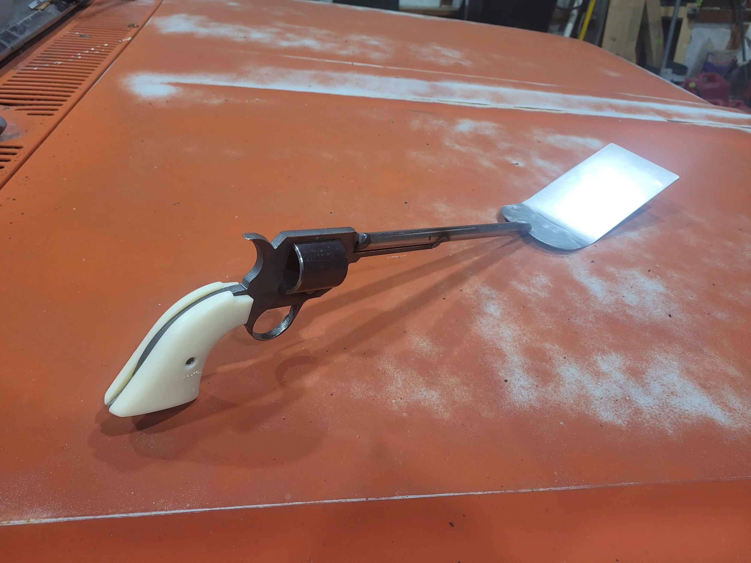 A custom spatula for grilling and cooking resting on a dusty orange surface with white paint spots and dust.