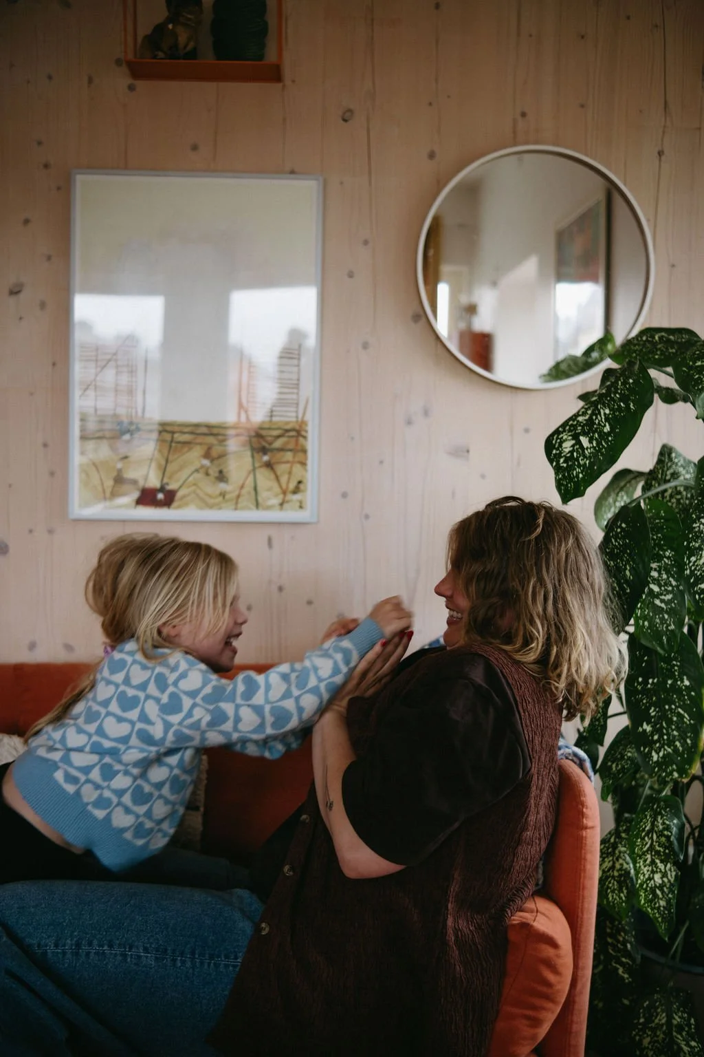 En mamma och ett barn leker och skrattar tillsammans i ett vardagsrum.