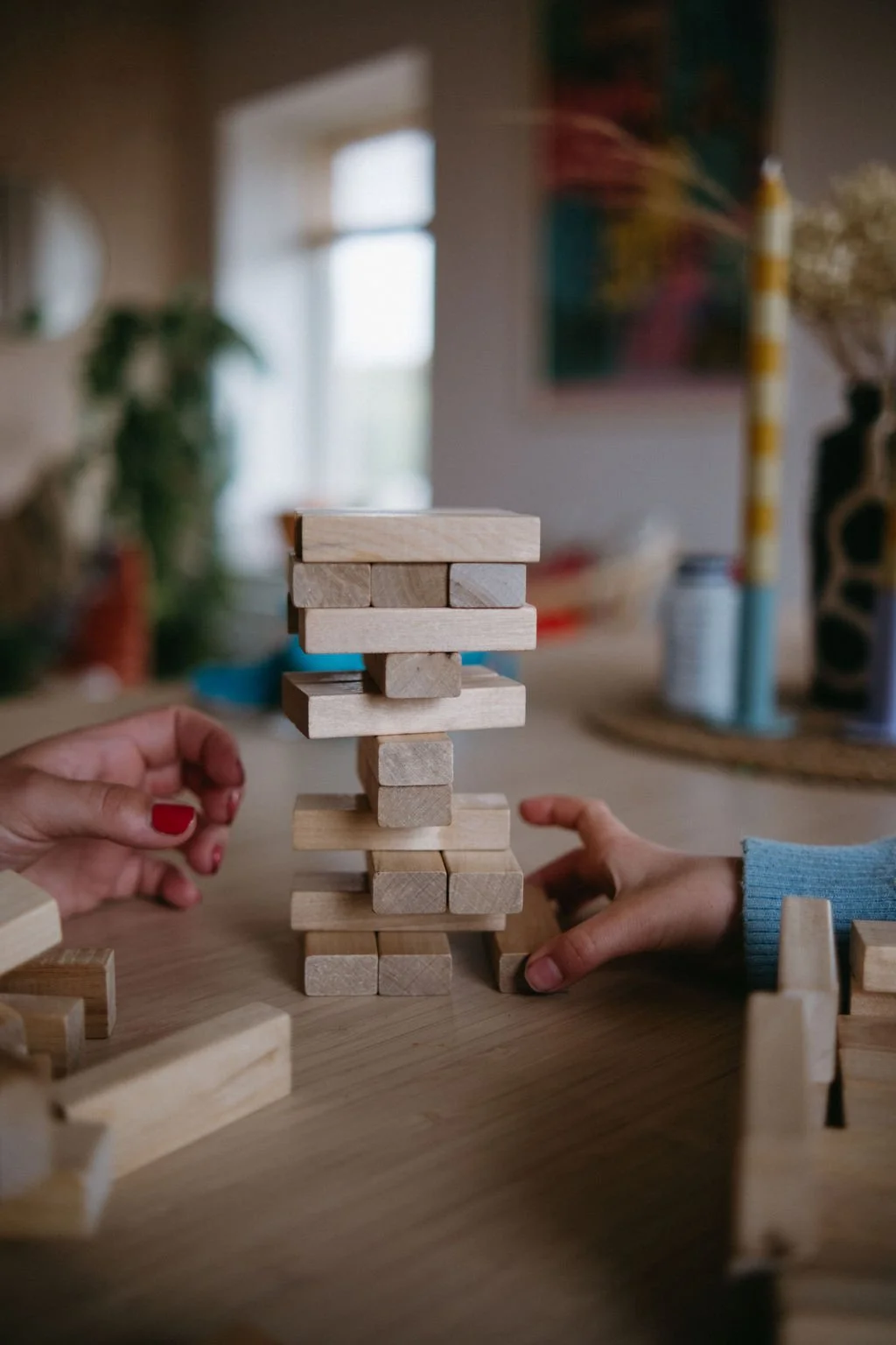 Två händer spelar ett träspel med en ställning av träblock, på ett bord i ett rum med blurrad bakgrund.