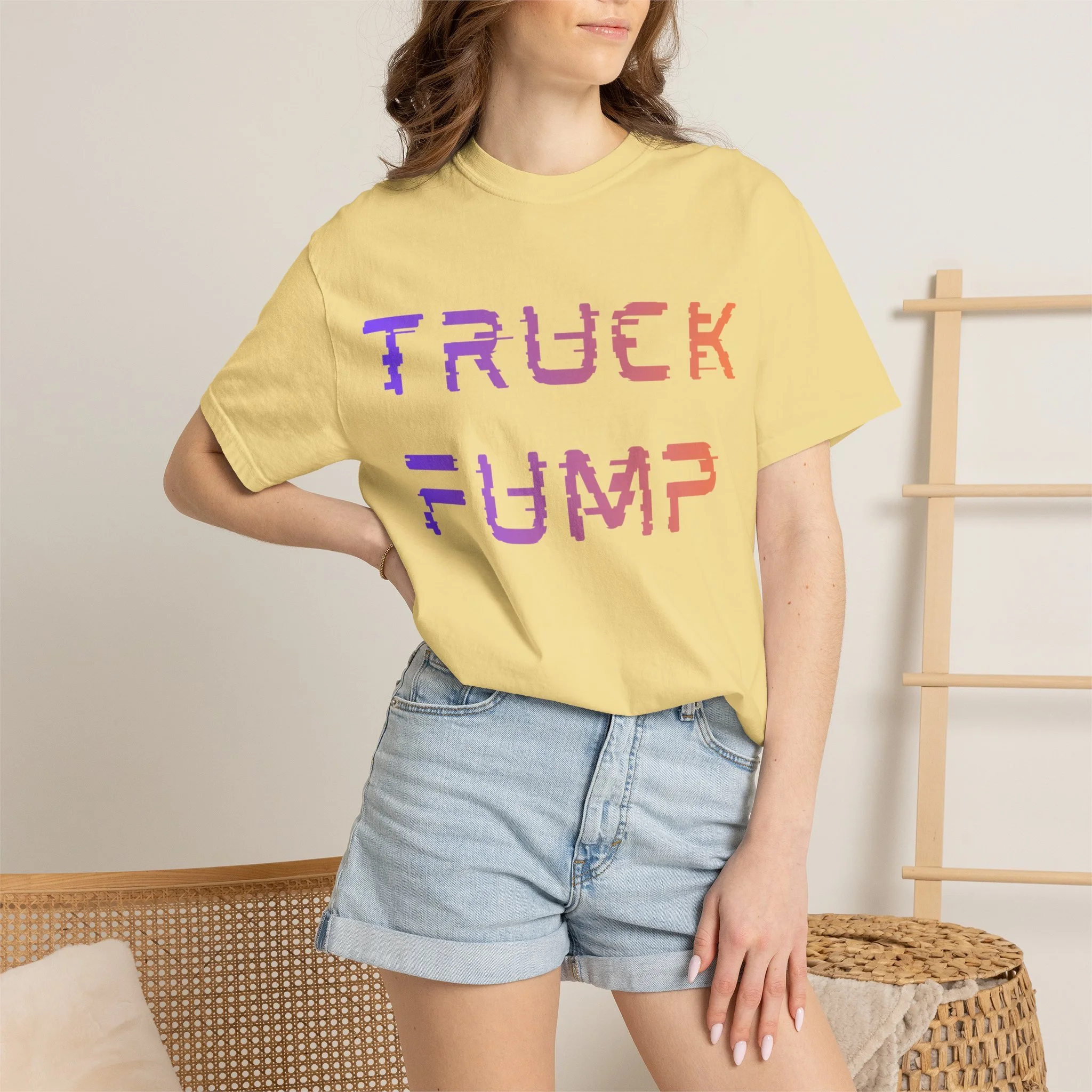 A woman wearing a yellow T-shirt with the word "TRUCK" in pixelated style, paired with denim shorts, standing in a room with neutral walls, next to a woven basket and a wooden ladder.