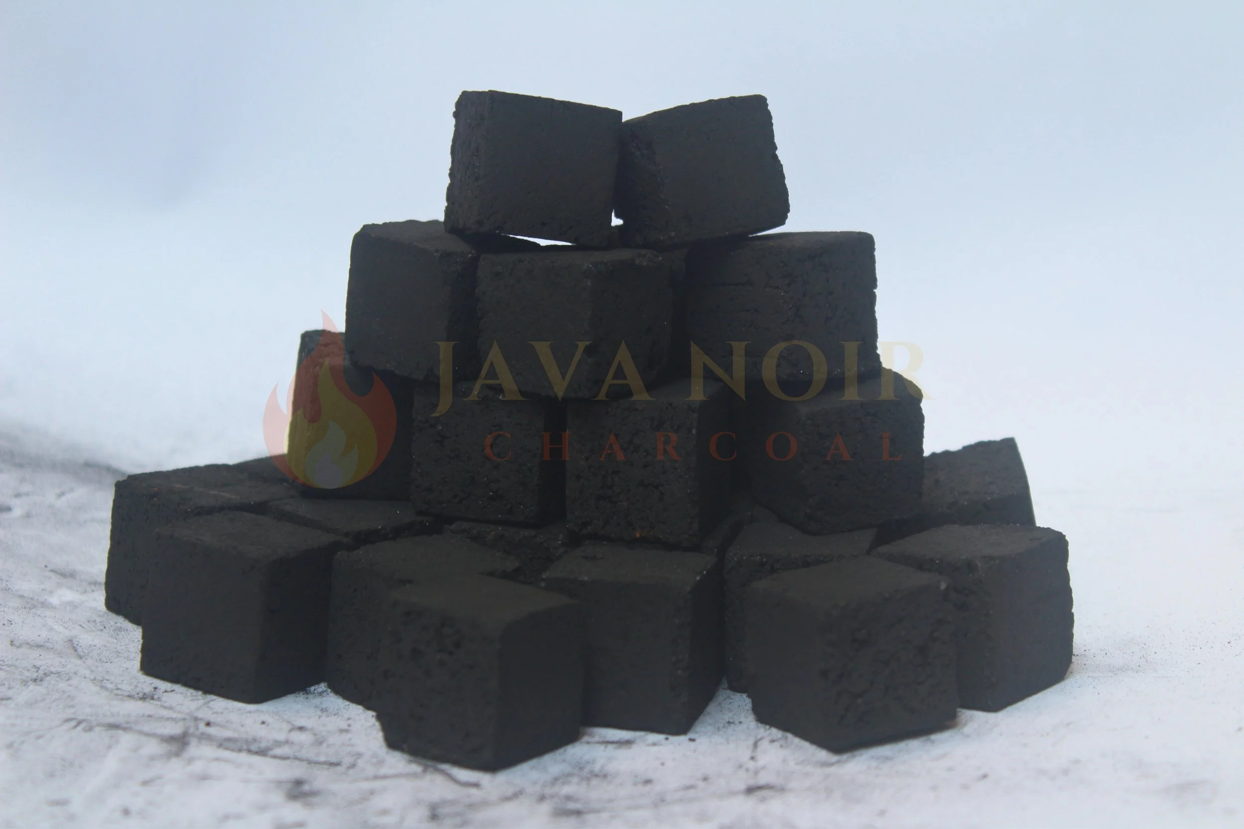 Stacked black charcoal briquettes on a snowy surface, with a blurred background.