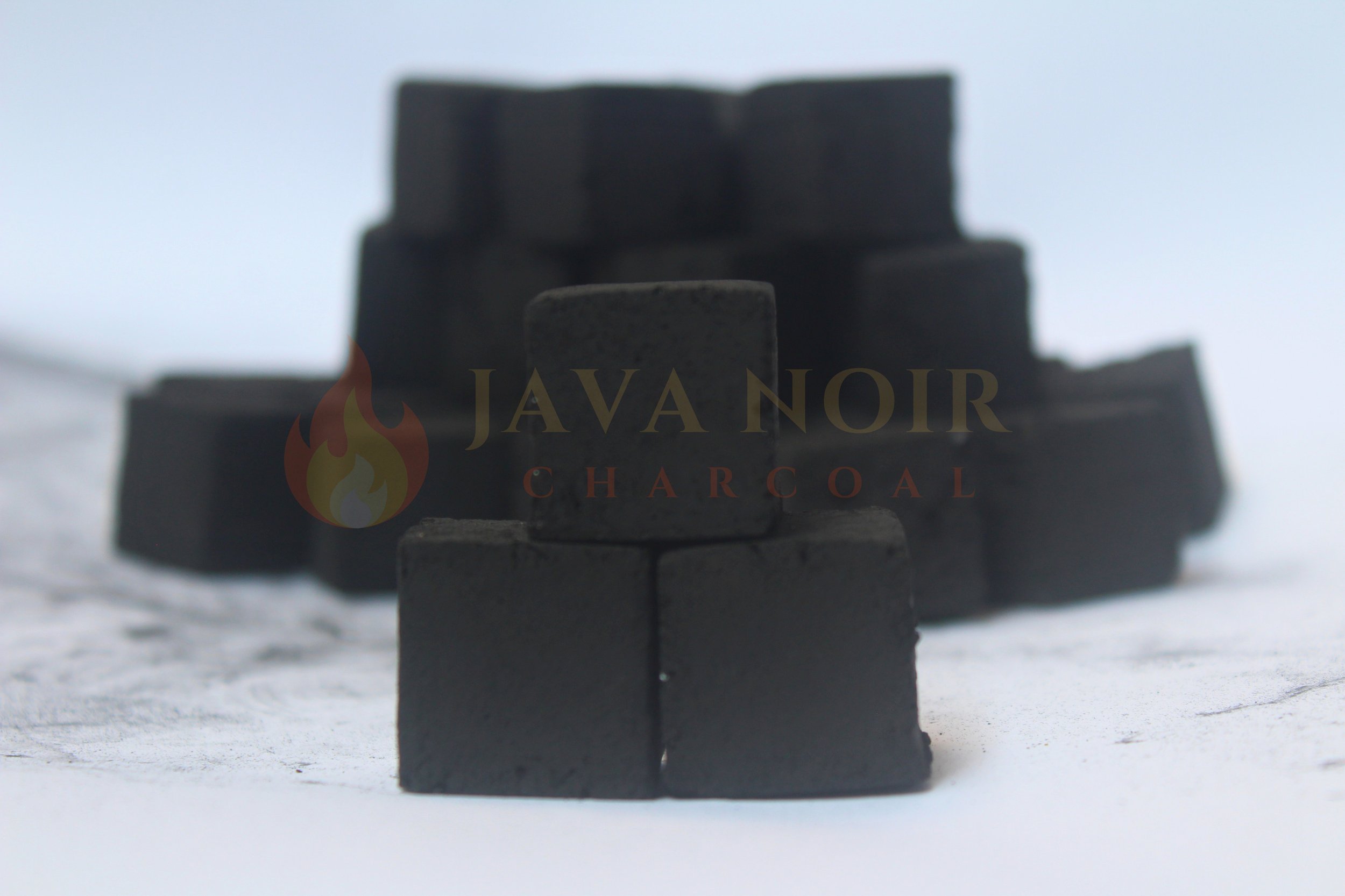 Stacks of charcoal briquettes with a logo reading 'Java Noir Charcoal' on the front, placed outdoors on snow with a clear sky in the background.