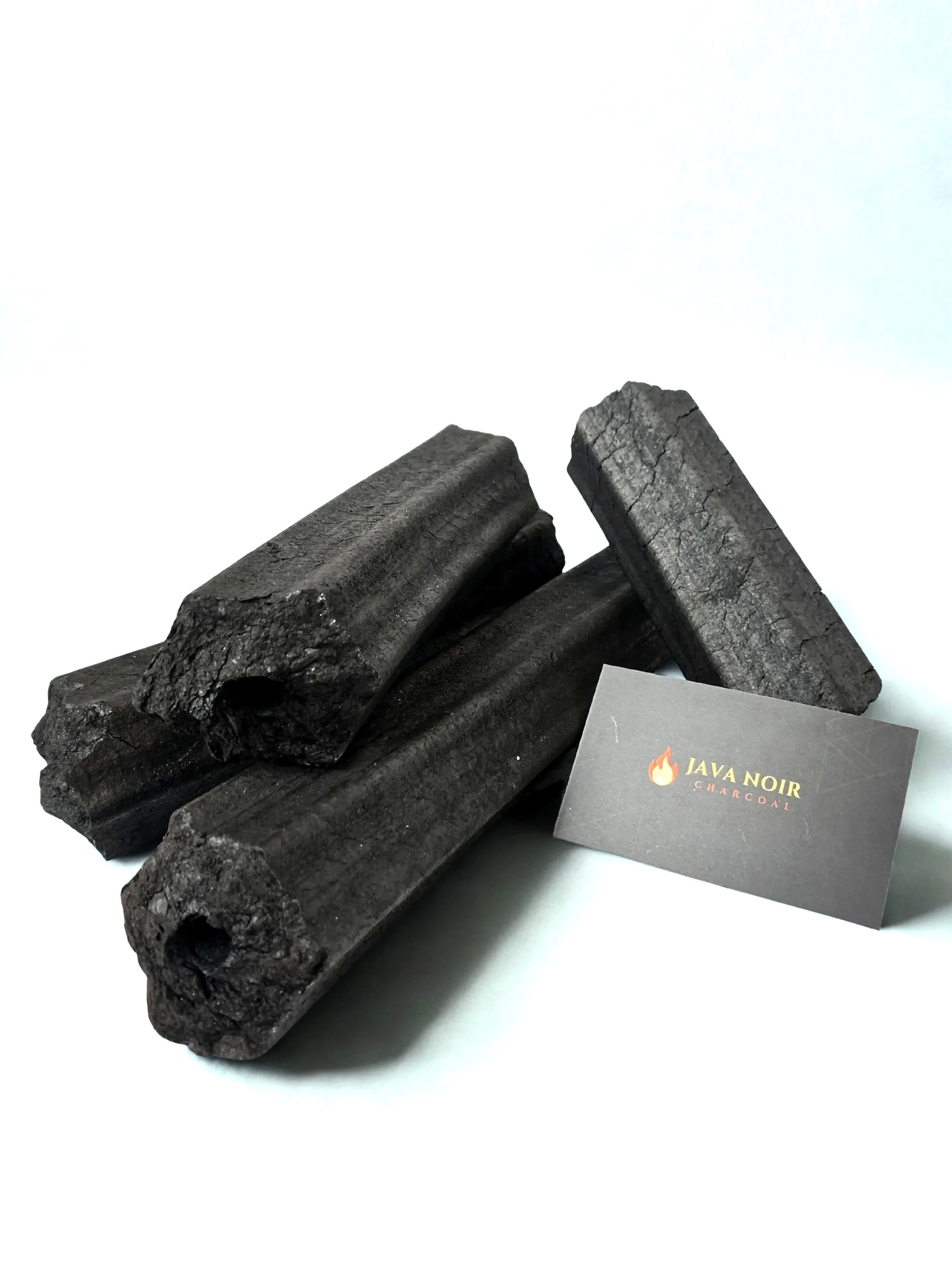 Several pieces of black charcoal and a business card with the logo 'Java Noir Charcoal' on a white background.