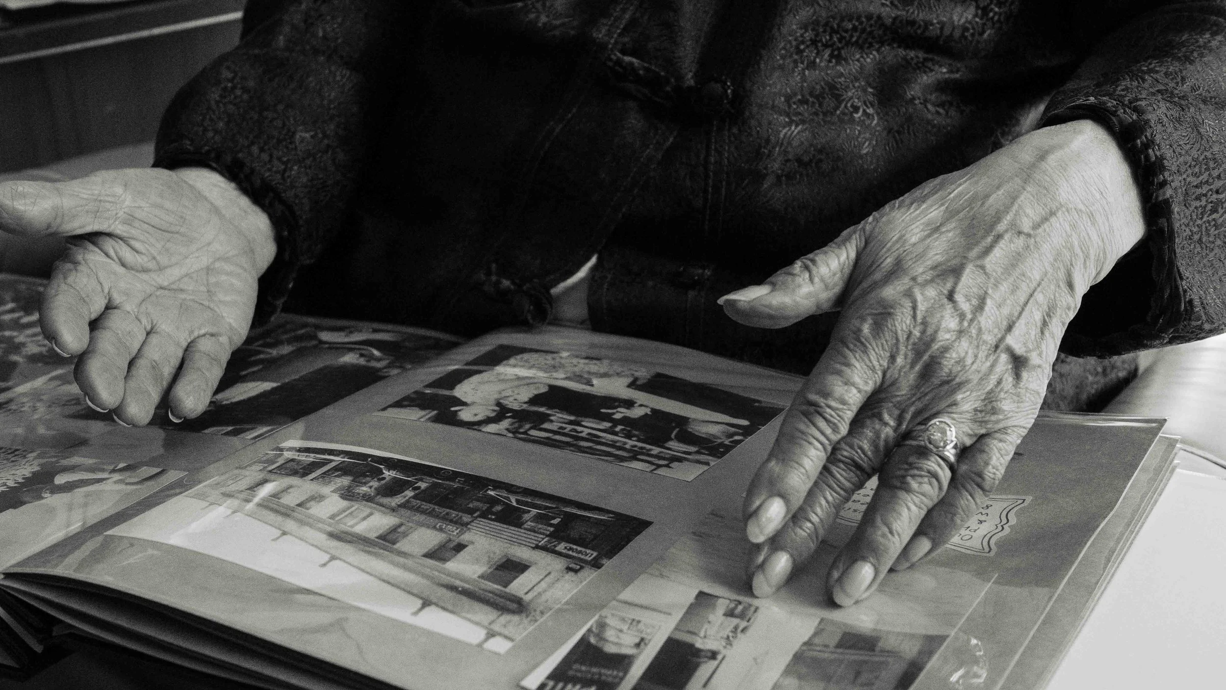 Close-up black and white photo of elderly hands resting on a photo album, pointing at pictures.