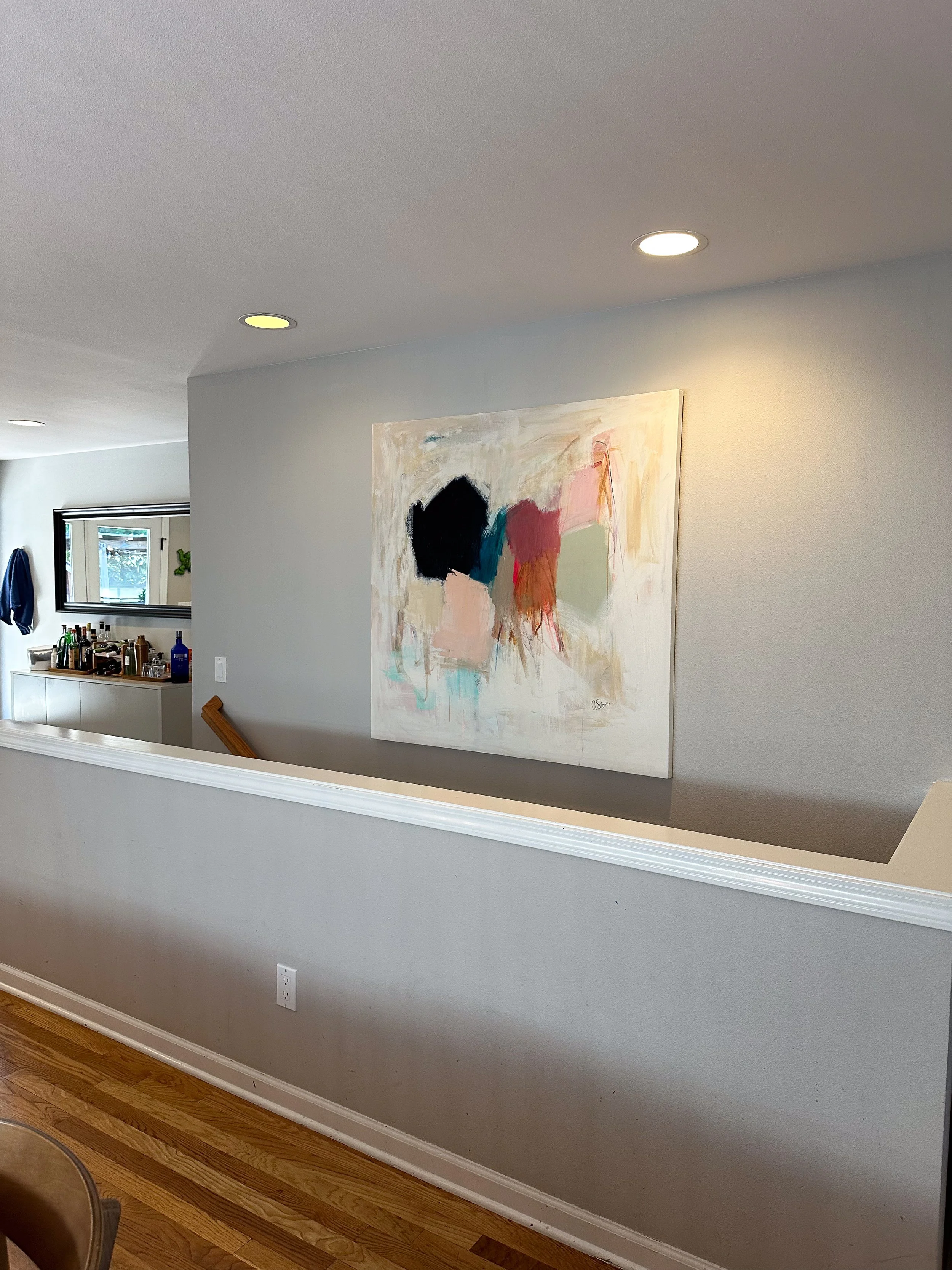 A modern interior with gray walls and ceiling, featuring a large abstract painting with soft pastel colors. In the background, there is a bar area with bottles and a mirror on the wall.