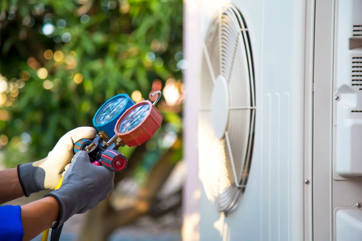 Person cleaning an air conditioning unit outside with a spray gun.