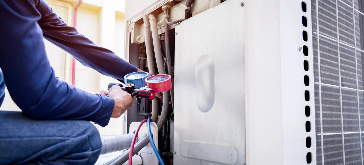 Person using a manifold gauge set to service an air conditioning unit outdoors.