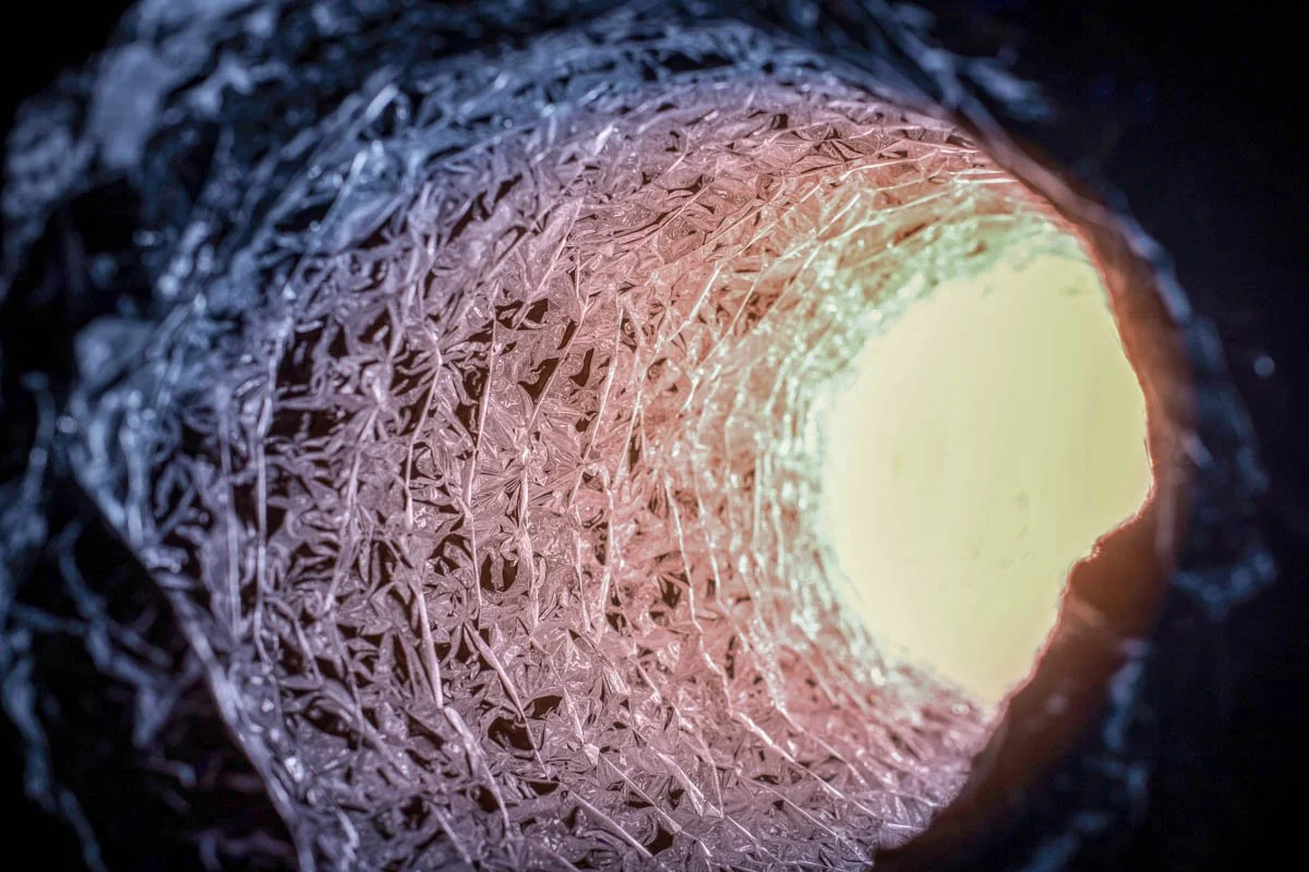View inside a frosty metal pipe with ice formations and light coming from the opposite end.