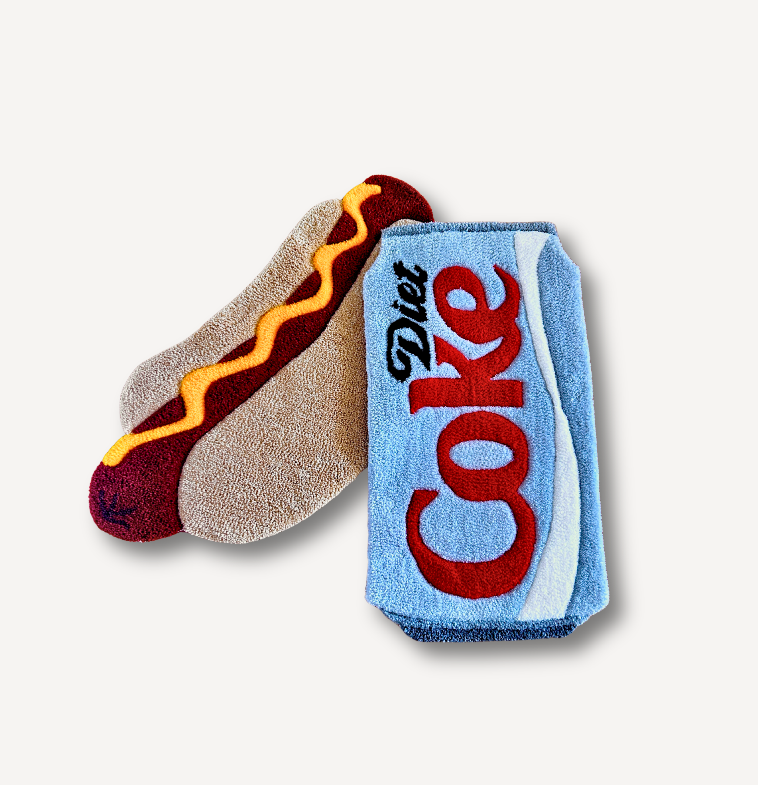 Close-up of two rugs, one shaped like a hot dog with mustard, and the other resembling a soft drink cup with a straw, placed on a plain gray background.