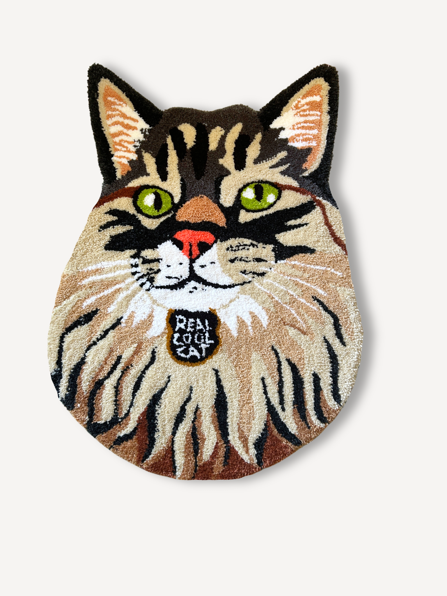 A rug in the shape of a cat's face with detailed fur patterns, green eyes, a pink nose, and a collar with a tag that says 'PEA COOL CAT'.
