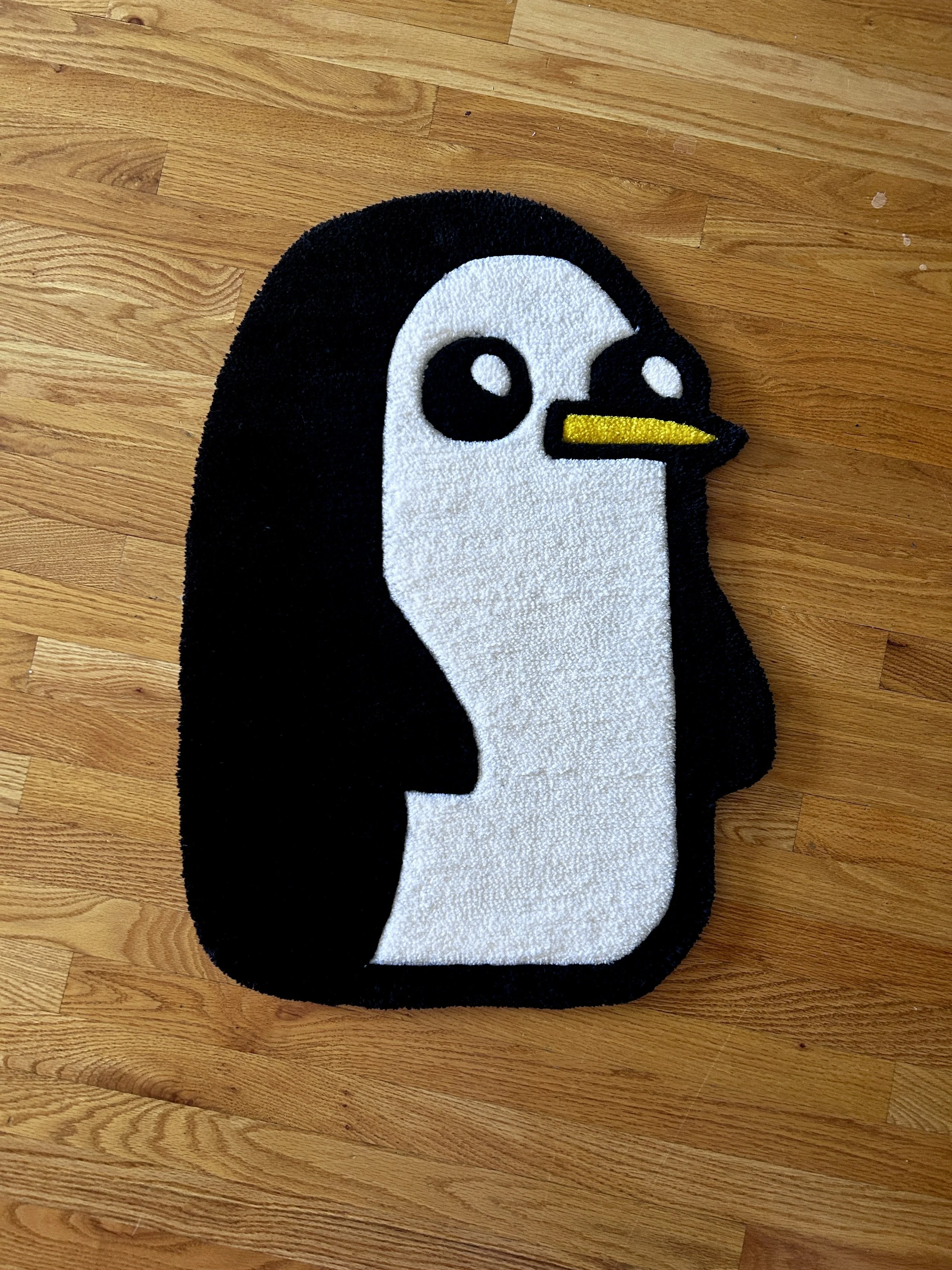 A penguin-shaped doormat with black, white, and yellow colors on a wooden floor.