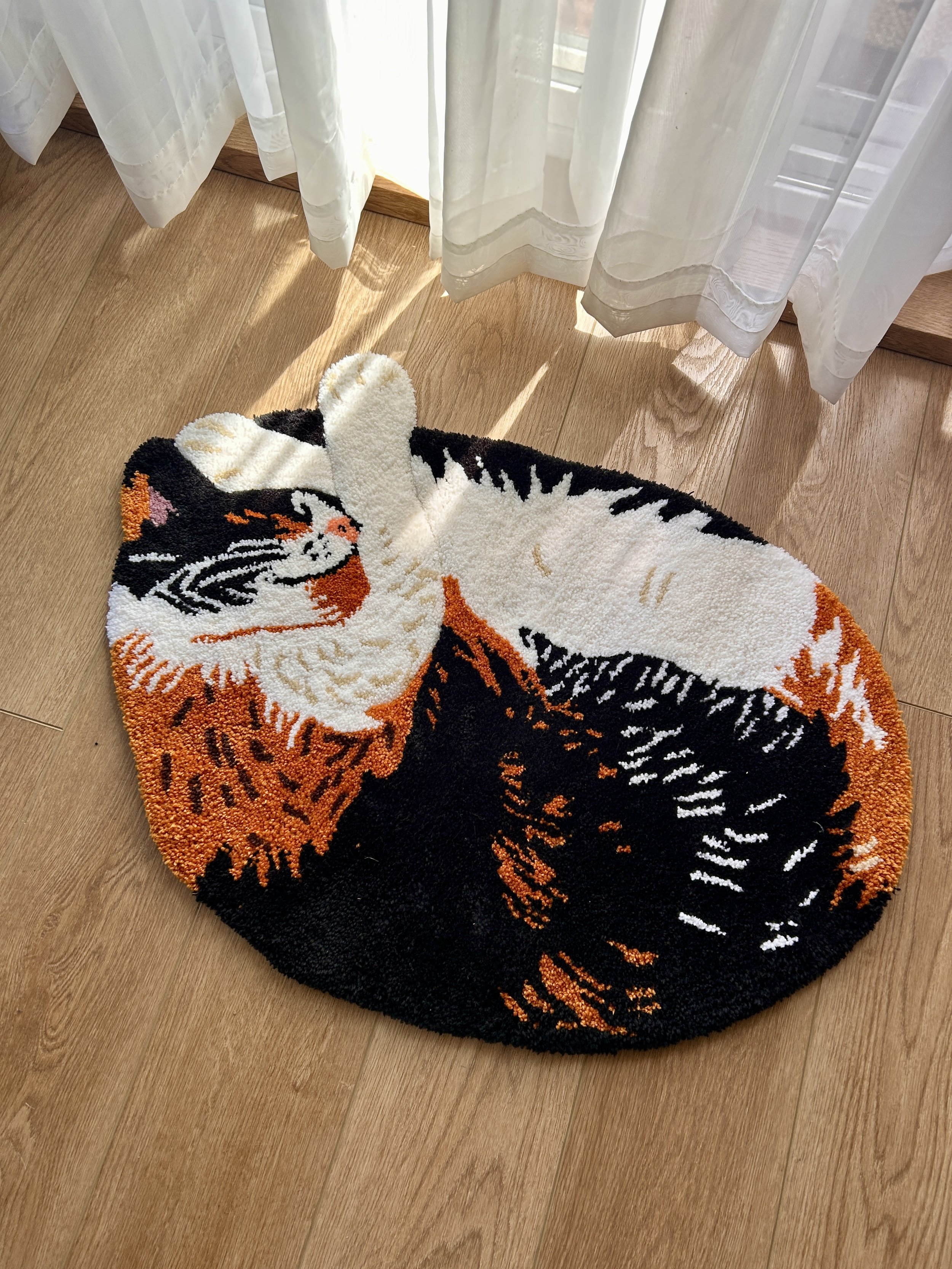 Close-up of a tiger-shaped rug on a wooden floor, with sheer white curtains and window letting in sunlight in the background.