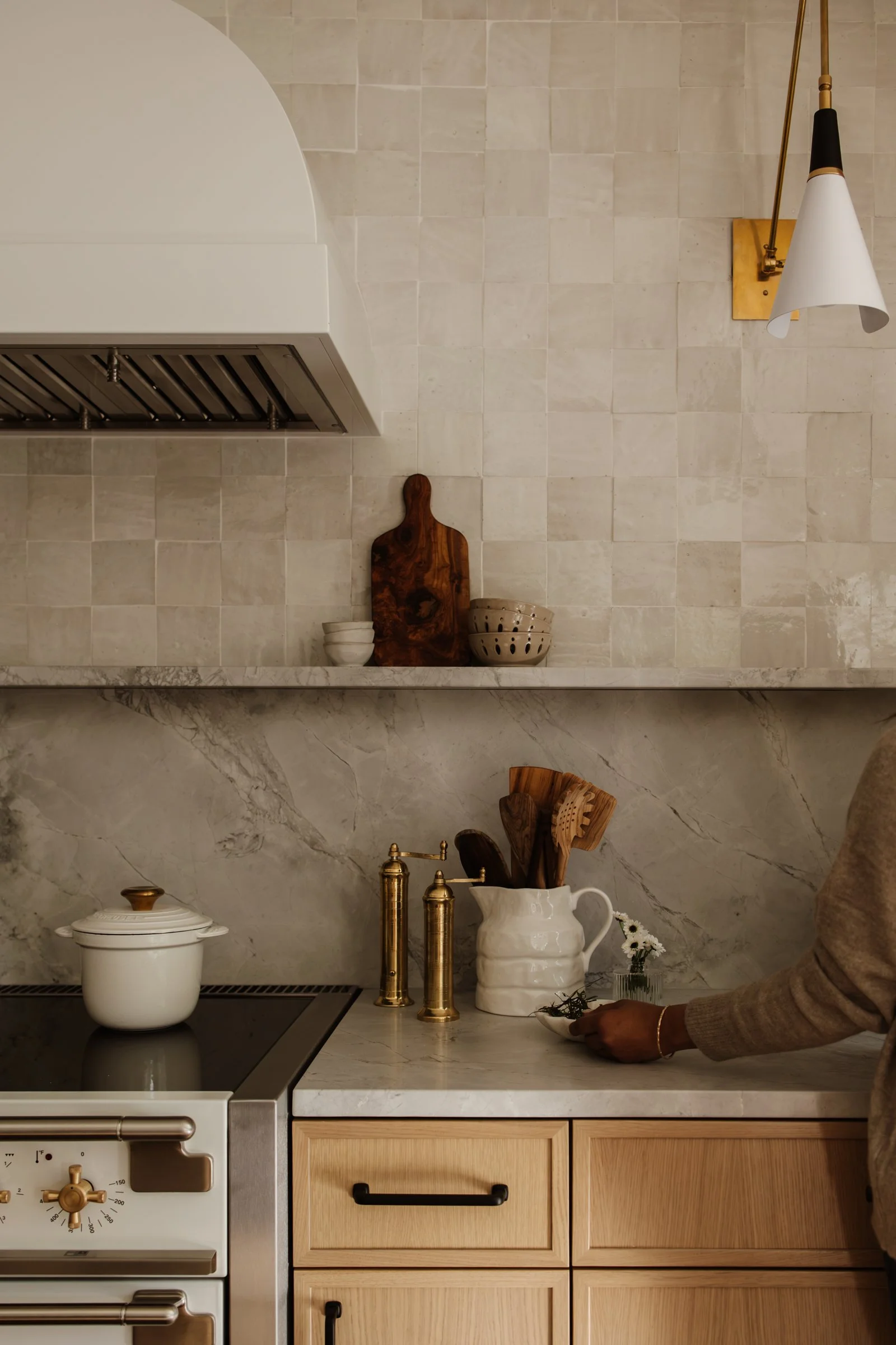 Kitchen scene with a person preparing herbs, featuring a marble countertop, wooden cabinetry, and decorative bowls and cutting boards on the wall.