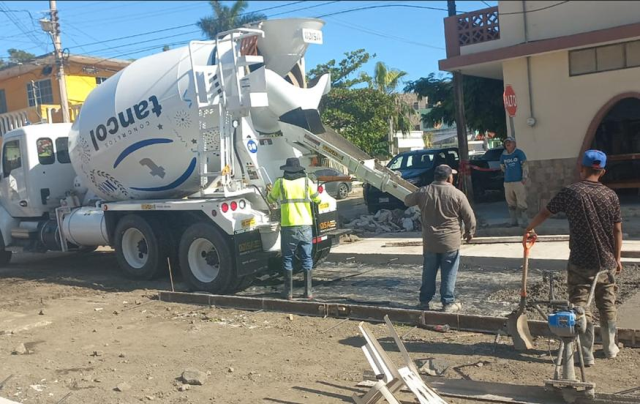 Trabajadores y un camión de concreto en una obra de construcción en una calle urbana.