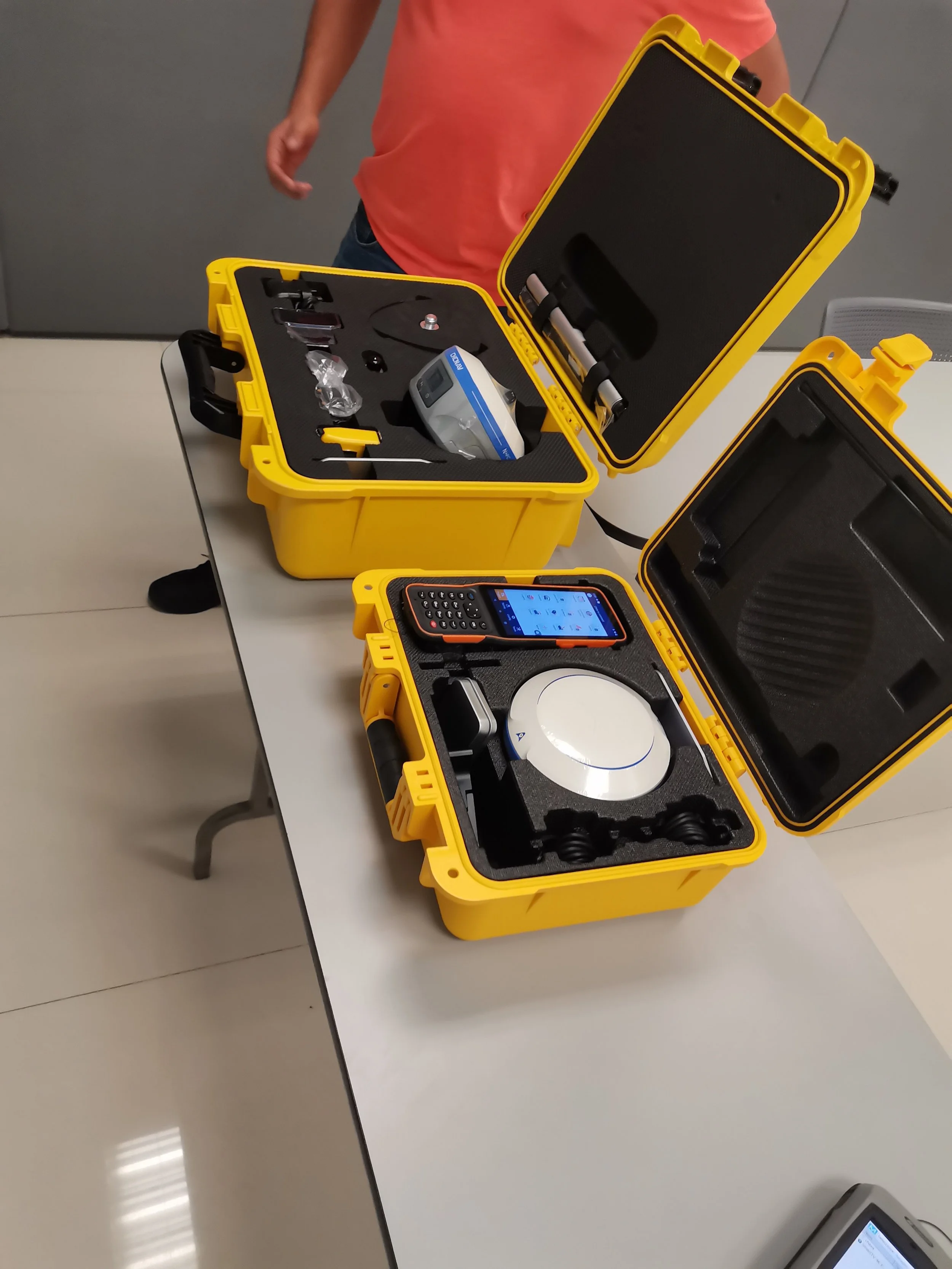 Conjunto de equipos médicos y herramientas tecnológicas en cajas de color amarillo en una mesa, incluyendo un monitor, un teléfono inteligente, y otros instrumentos médicos.