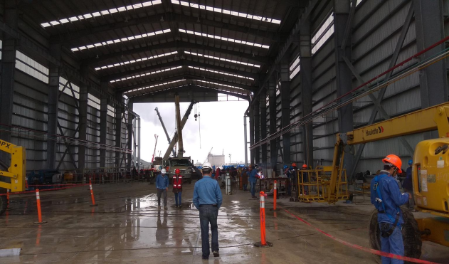 Trabajadores en un aeropuerto o hangar industrial, con maquinaria y equipo de construcción, en un ambiente cerrado y húmedo.