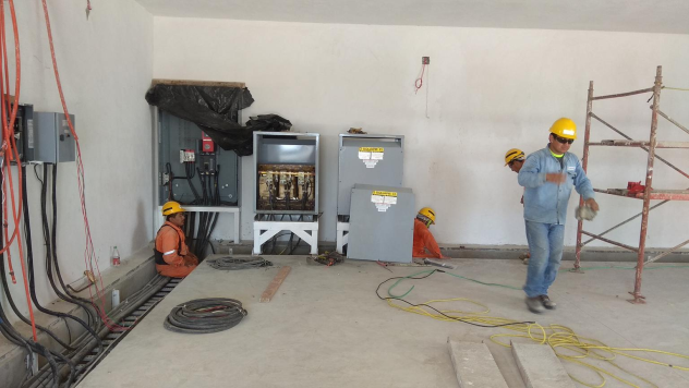 Trabajadores de construcción en una obra, usando cascos, en un ambiente interior con herramientas y estructura en desarrollo.