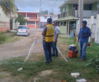 Tres personas en un campo de césped, con herramientas y equipo de medición, en una zona residencial.