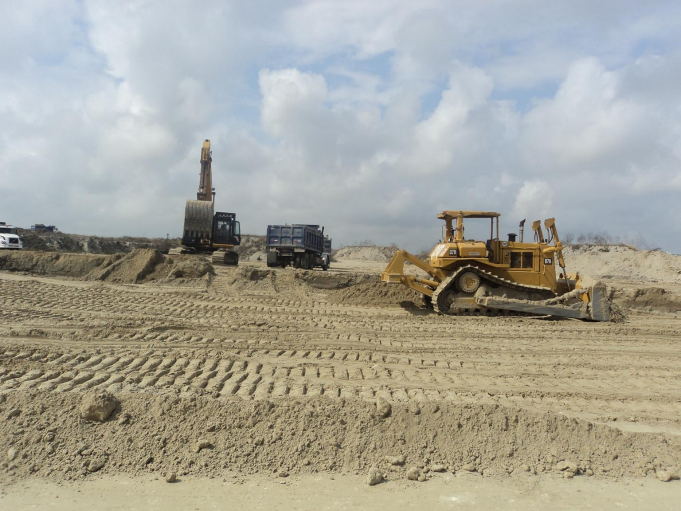 Maquinaria pesada en un sitio de construcción de tierra o arena, con un cielo nublado en el fondo.