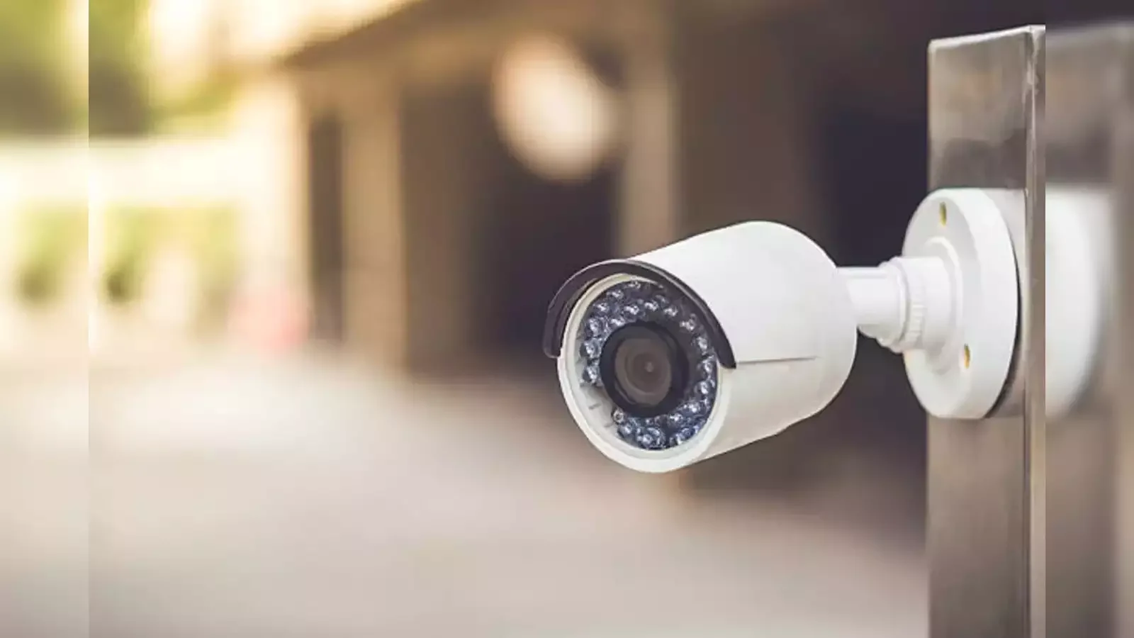 A white security camera mounted on a metal surface outdoors.