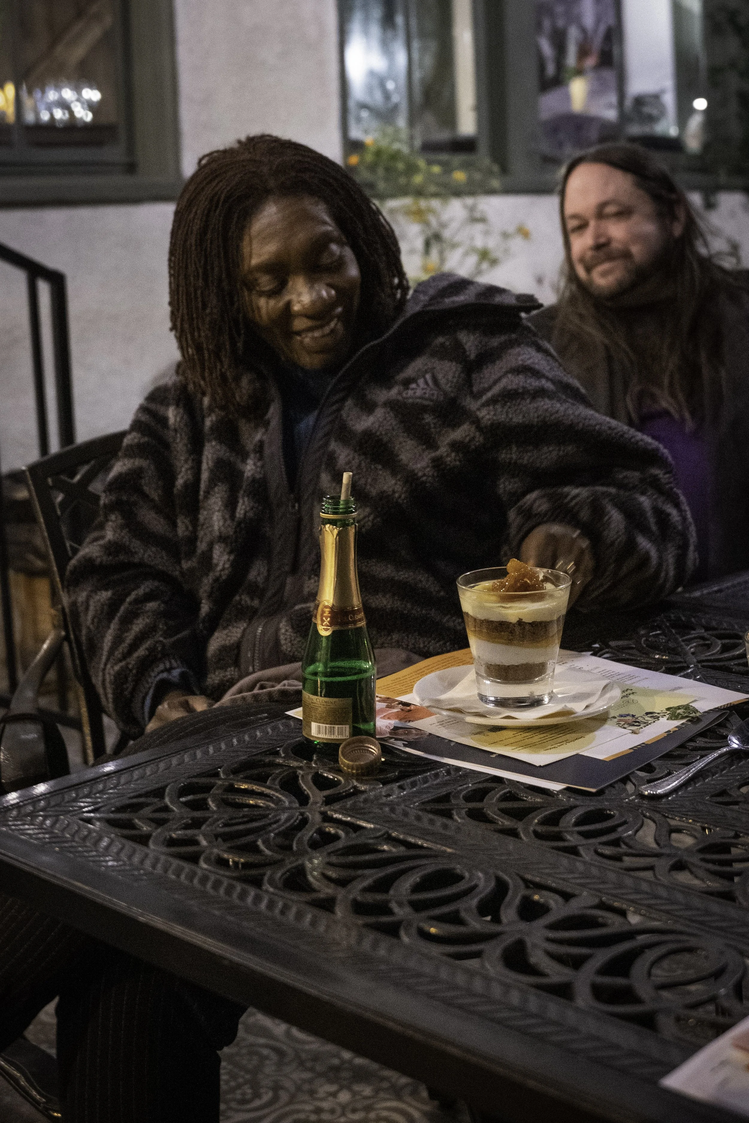  Two attendees relaxing at an ornate outdoor table with drinks and dessert during an evening film event. 