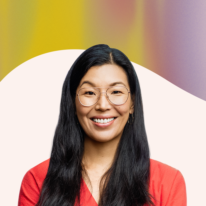 Ai-jen Poo - President, Give Not Take Media - Smiling woman with long black hair, wearing glasses and a red top, against an abstract colorful background.