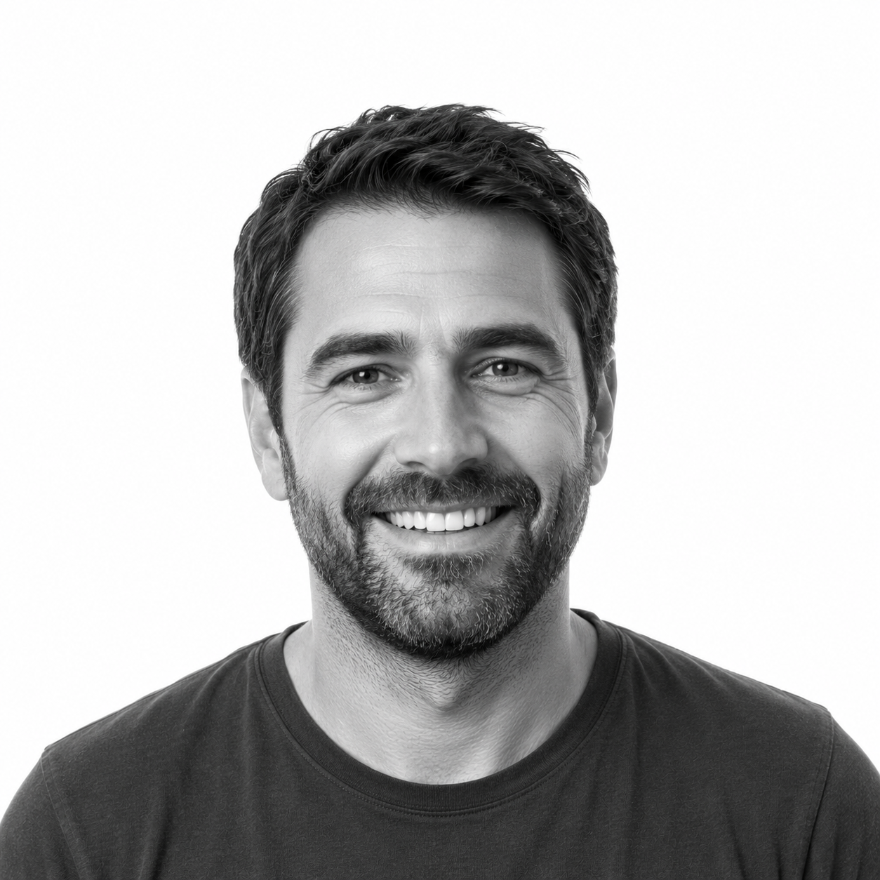 A smiling man with dark hair and a beard, wearing a dark t-shirt, against a plain white background.