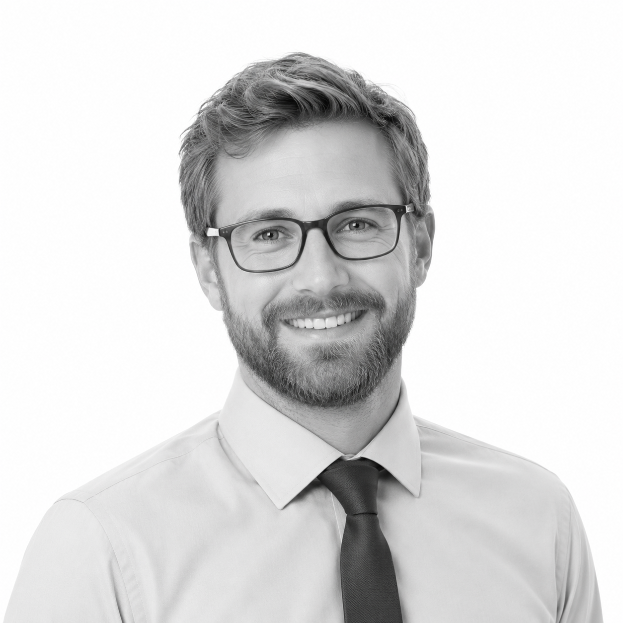 Black and white portrait of a smiling man with glasses, beard, light shirt, and dark tie, against a plain background.