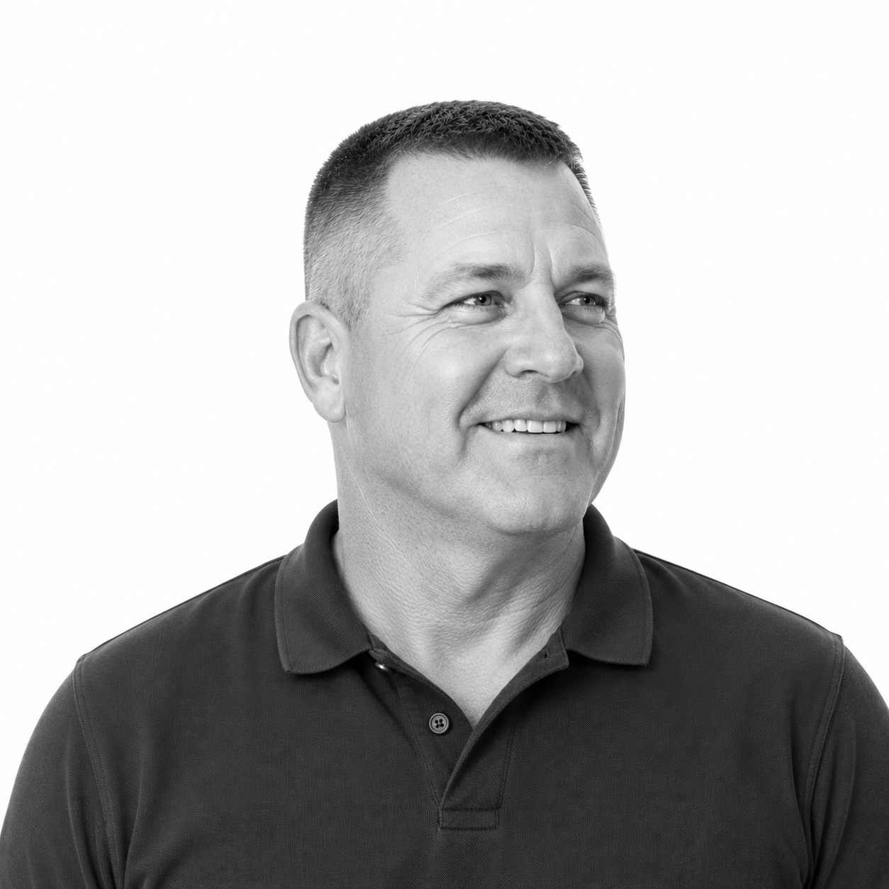 Black and white photo of a smiling man with short hair, wearing a collared shirt, looking to his right.
