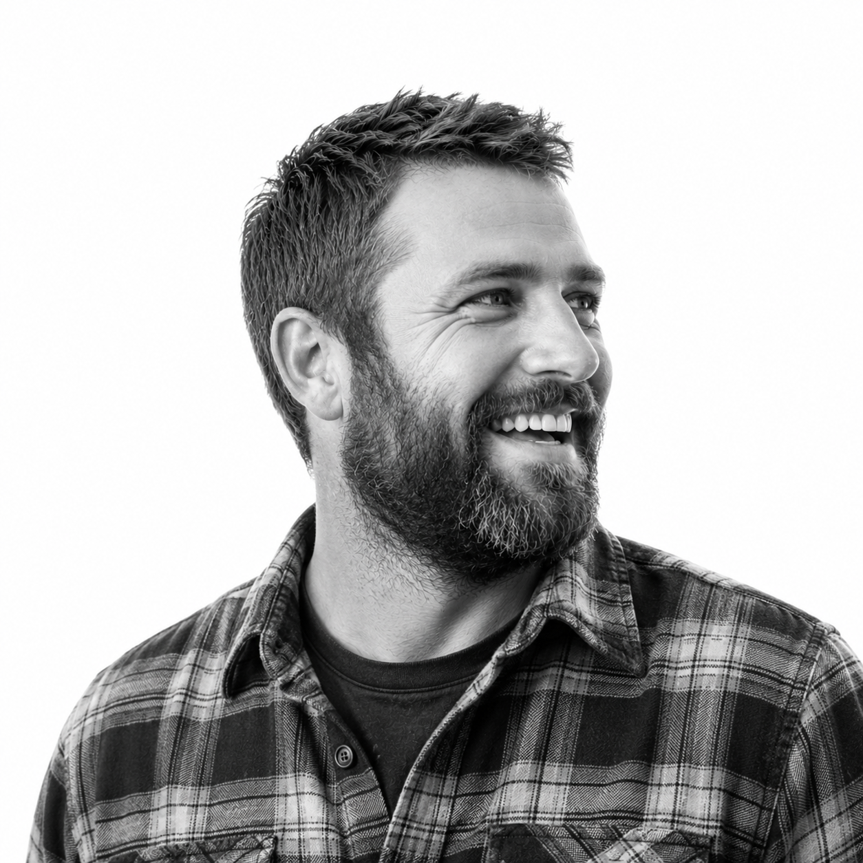 Black and white photo of a smiling man with a beard and short hair, wearing a checkered shirt, looking to the right.