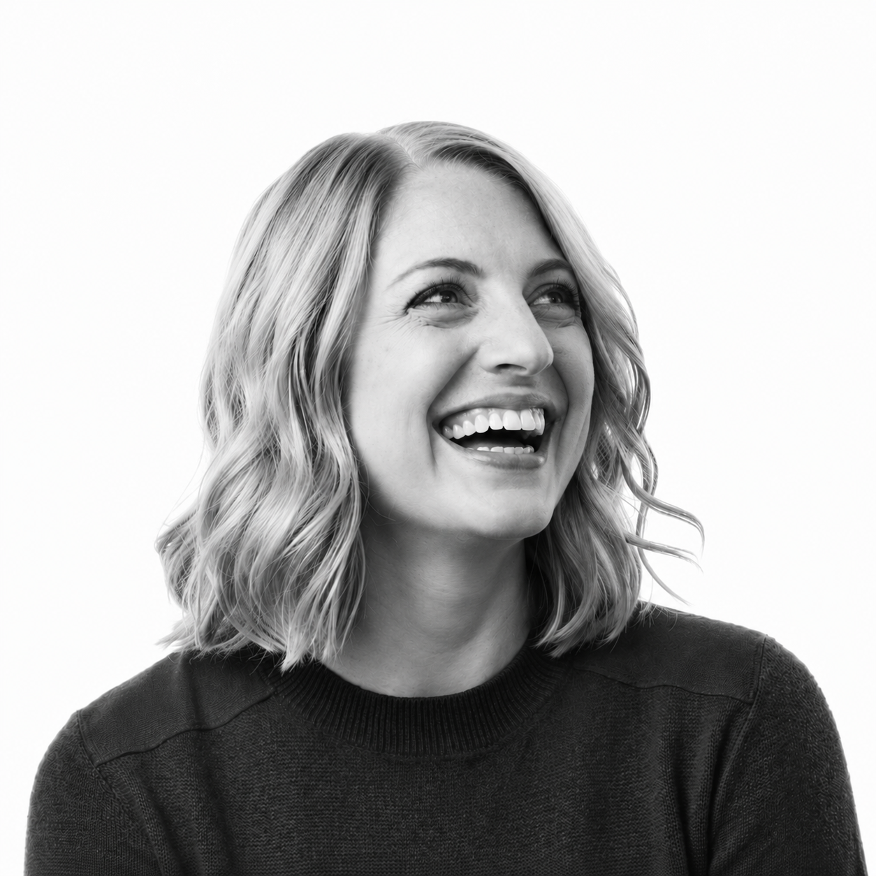 Black and white portrait of a young woman with wavy, shoulder-length hair, smiling and looking upward, wearing a dark sweater, against a plain white background.