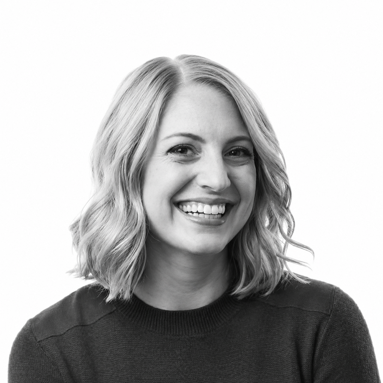 Black and white portrait of a smiling woman with wavy shoulder-length hair, wearing a dark sweater, against a plain white background.