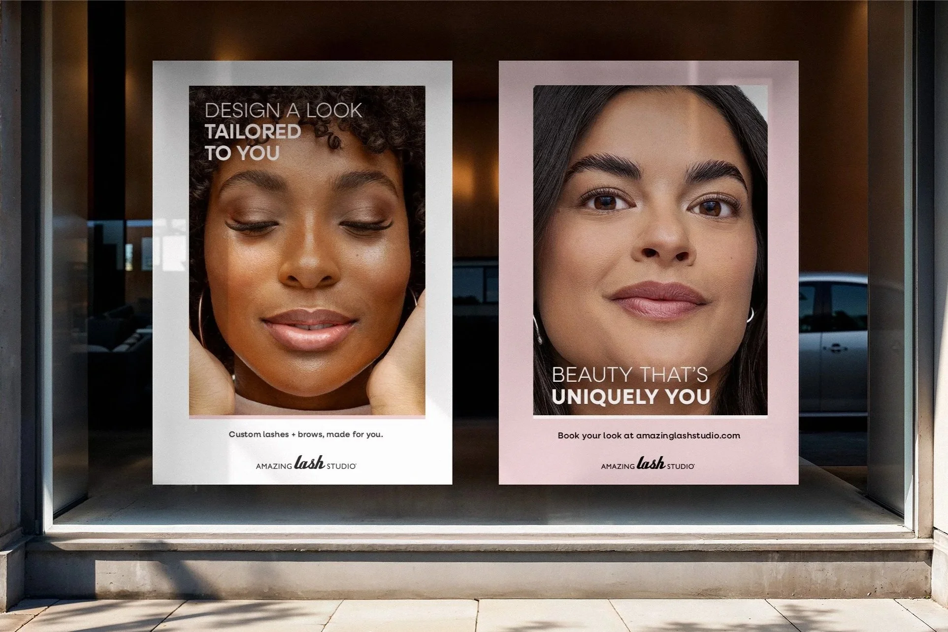 Two Amazing Lash Studio window posters in a storefront: the left reads “Design a look tailored to you,” and the right reads “Beauty that’s uniquely you. Book your look at amazinglashstudio.com.