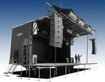 Empty outdoor stage with sound equipment and a few people standing nearby.
