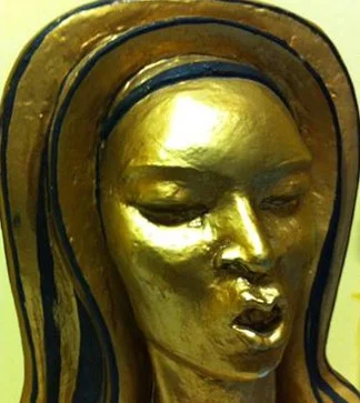 Close-up of a gold-colored sculpture of a woman's face with her eyes closed and lips slightly parted.