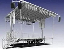 Large outdoor stage with a roof, metal framework, and railing, set up on a flat trailer or platform.