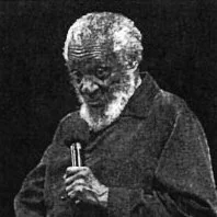 Old man with white hair and beard speaking into a microphone