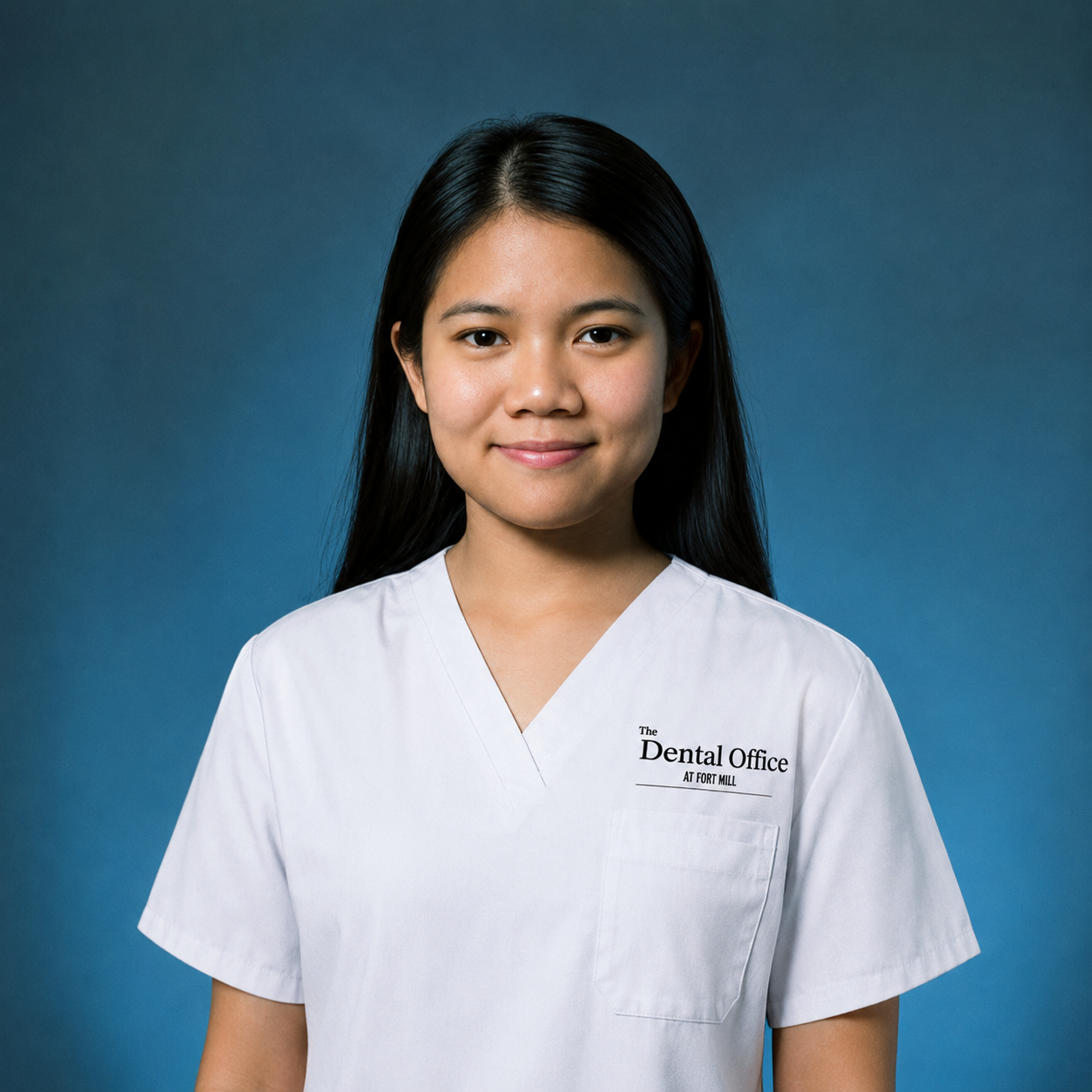 Young Asian woman in dental office uniform smiling at camera against blue background.
