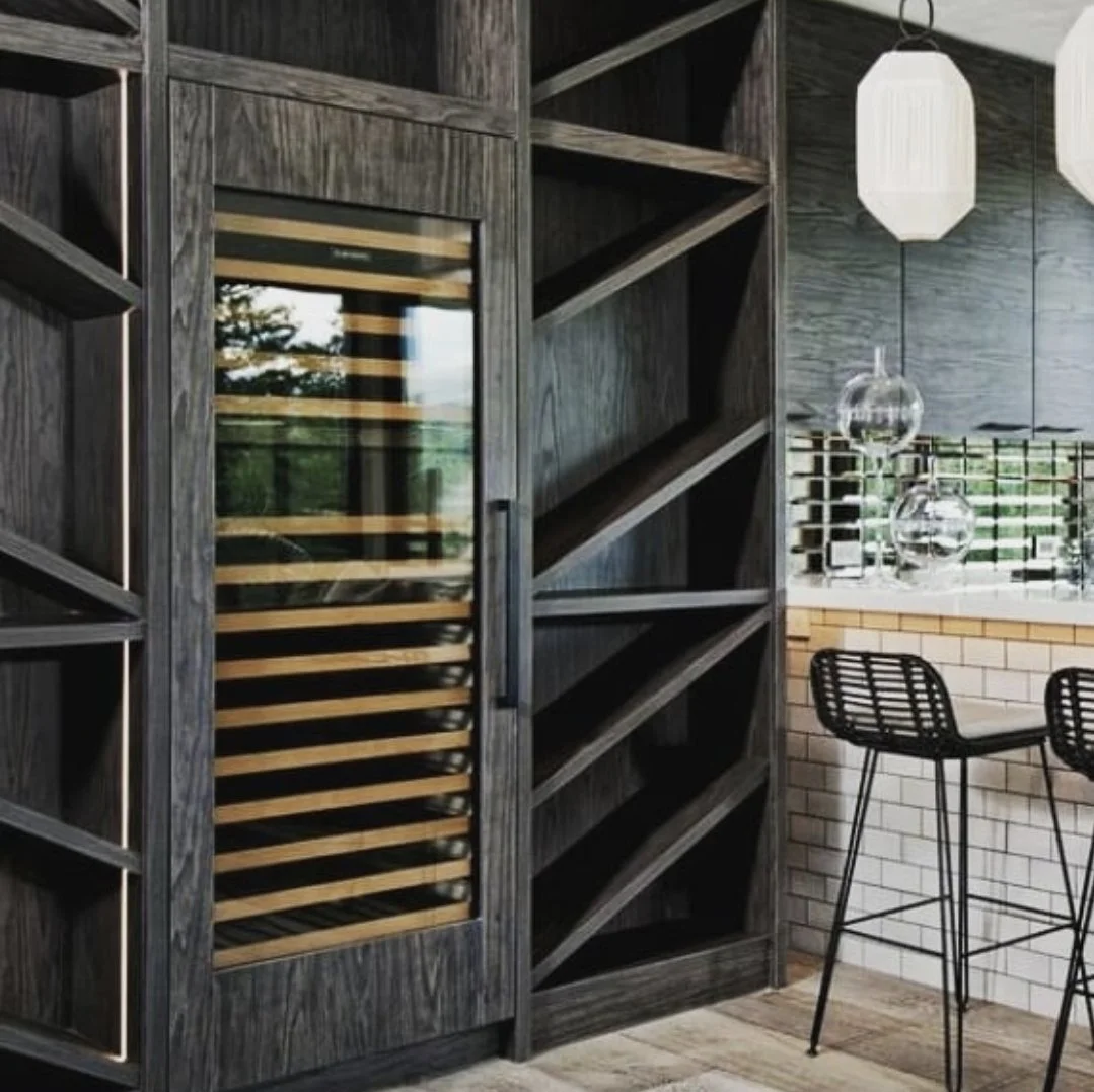 Modern bar area with dark wood wine fridge and open shelving, bar stools, pendant lights, and window with decorative grid